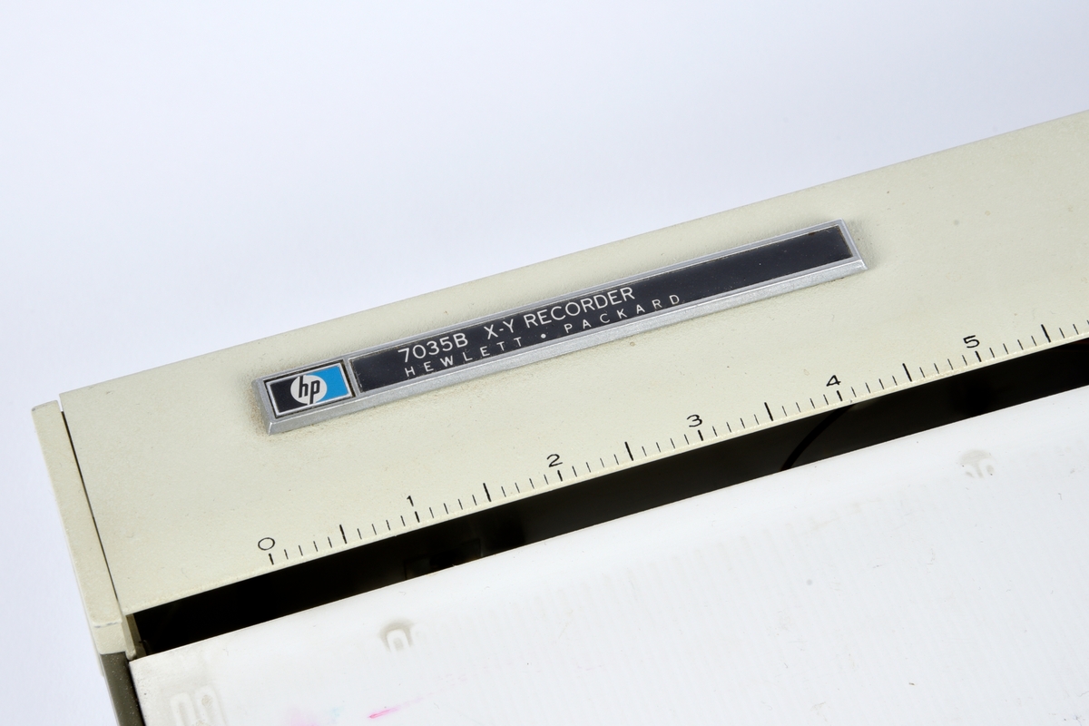 Testutstyr bestående av en plotter med tilhørende plotterpapir, plotterpenner, overtrekk, ledninger, elektriske plugger, overganger og et etui med skrivertilbehør. Alt oppbevart i en polstret transportkasse med lokk.