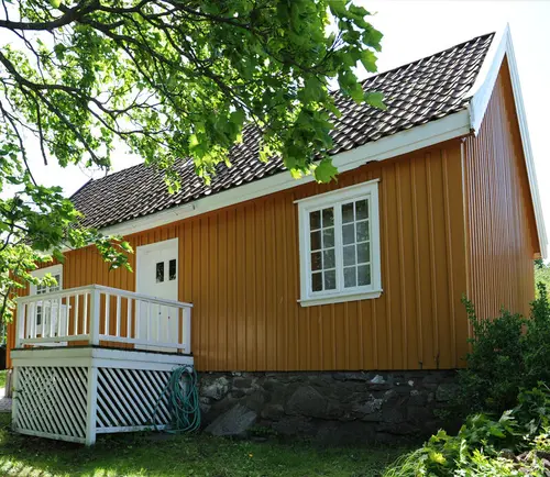 Bildet viser et gult hus med hvite karmer, i en grønn hage.