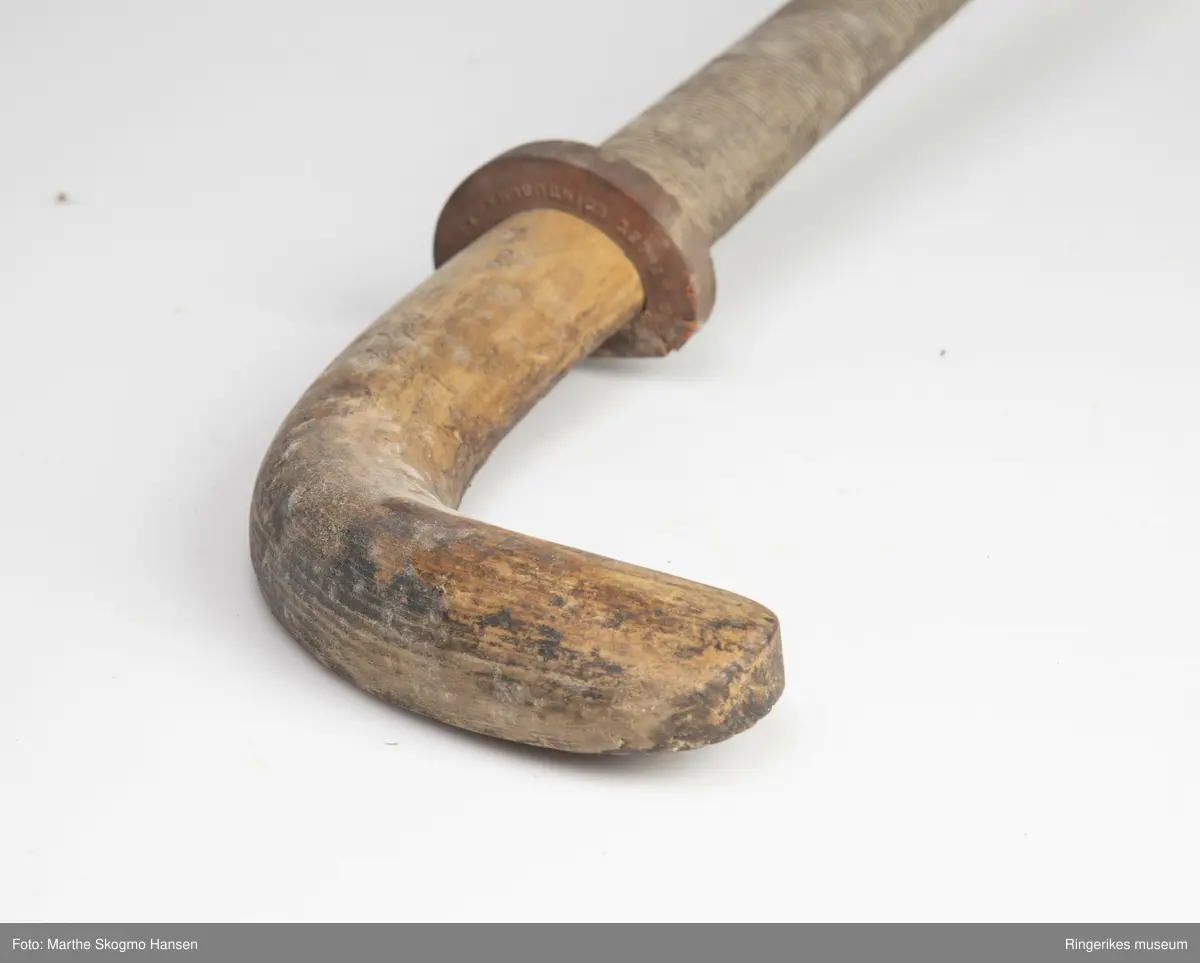 Hockeykølle i tre med rundt skaft og  kølle/slagdel som er flat på den ene siden og rund på den andre.Skaftet er dekket med tråd i to farger som er surret tett rundt skaftet.  I overgangen mellom skaft og kølle er det en rød gummiring.