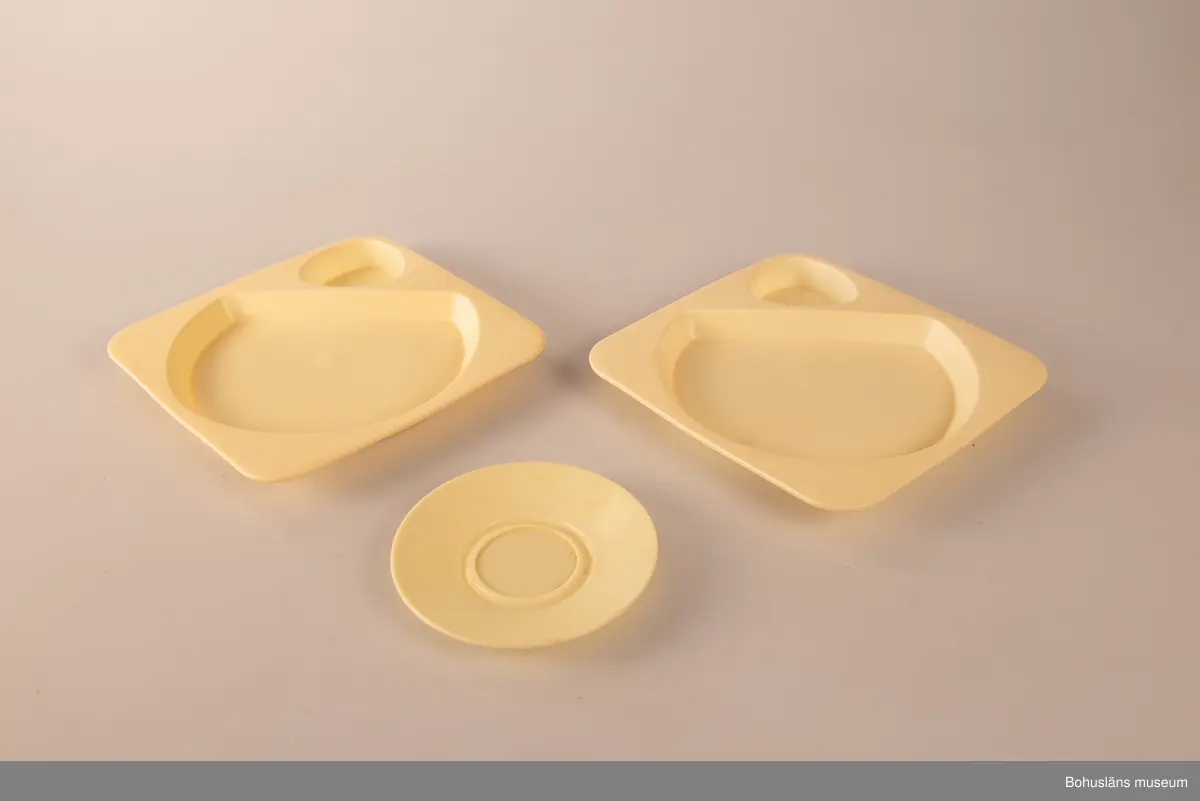 Tre plasttallrikar av formgjiten ljusgul plast. Två likadana stapelbara med fördjupning för ett trekantigt format plastglas (se UM031664) och en större yta för maten. I botten märkta HUSQVARNA MADE IN SWEDEN. Gult tefat, ursprungligen ett kaffefat.