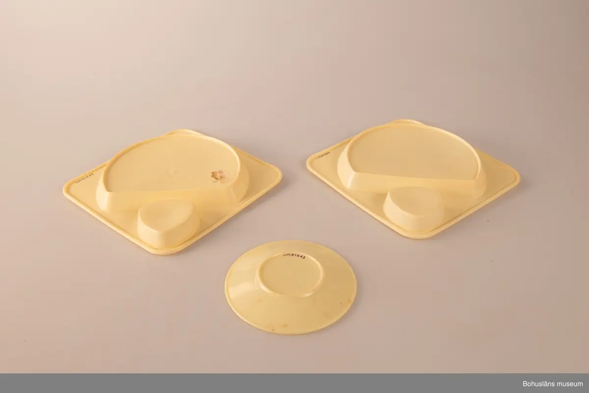 Tre plasttallrikar av formgjiten ljusgul plast. Två likadana stapelbara med fördjupning för ett trekantigt format plastglas (se UM031664) och en större yta för maten. I botten märkta HUSQVARNA MADE IN SWEDEN. Gult tefat, ursprungligen ett kaffefat.
