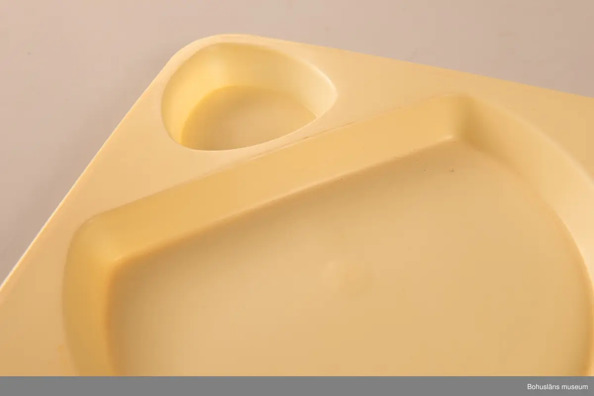 Tre plasttallrikar av formgjiten ljusgul plast. Två likadana stapelbara med fördjupning för ett trekantigt format plastglas (se UM031664) och en större yta för maten. I botten märkta HUSQVARNA MADE IN SWEDEN. Gult tefat, ursprungligen ett kaffefat.