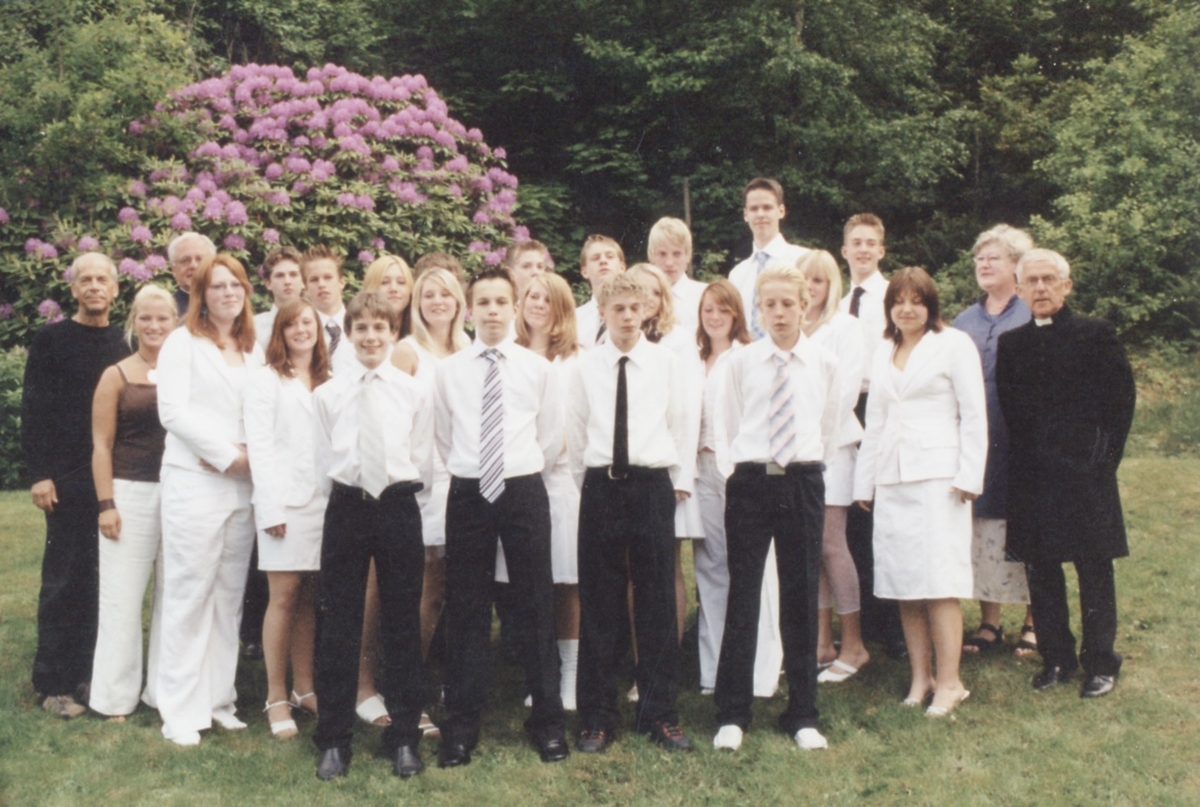 Konfirmationsdeltagare står på gräsmattan utanför Kållereds Missionskyrkan (senare Ekenkyrkan) år 2004. I bakgrunden ses en stor rhododendronbuske i full prakt. Andreas Karlsson (son till Peter Karlsson), som står till höger bredvid kvinnan i dräkt och pastorn, är fotografens barnbarn.