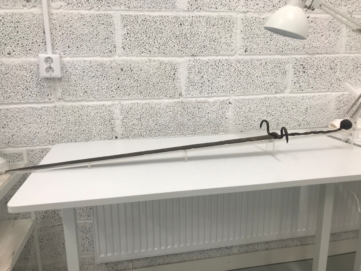 Dubbeleggat, närmast komplett svärd. Avslutas med en rund svärdskanpp som nu är löst fäst vid greppets tånge. Parerstången är böjd i två bågar.