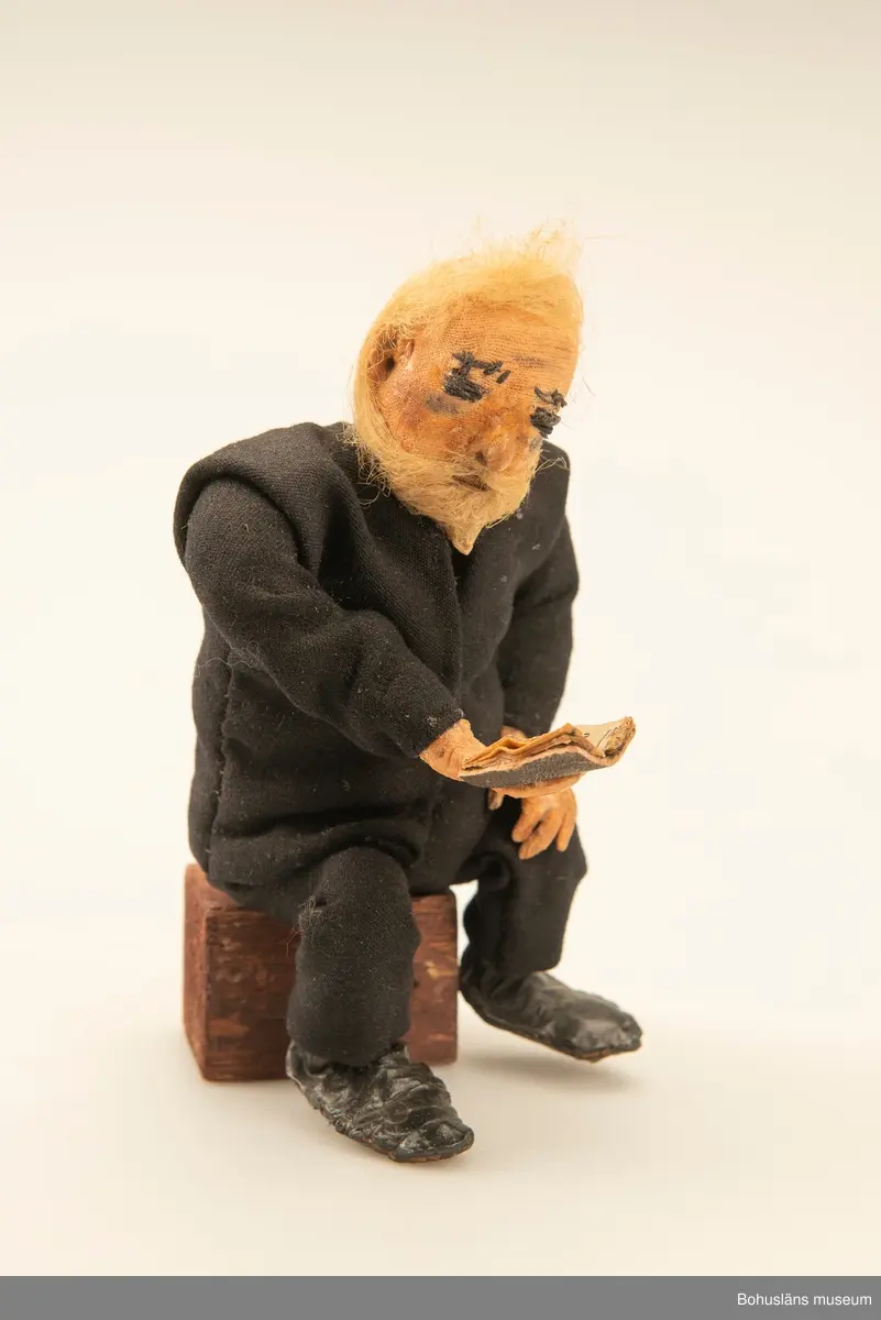 Gubbe med psalmbok sittande på en träkub