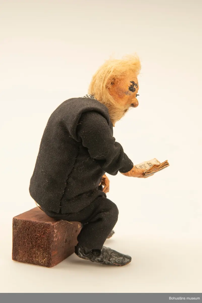 Gubbe med psalmbok sittande på en träkub