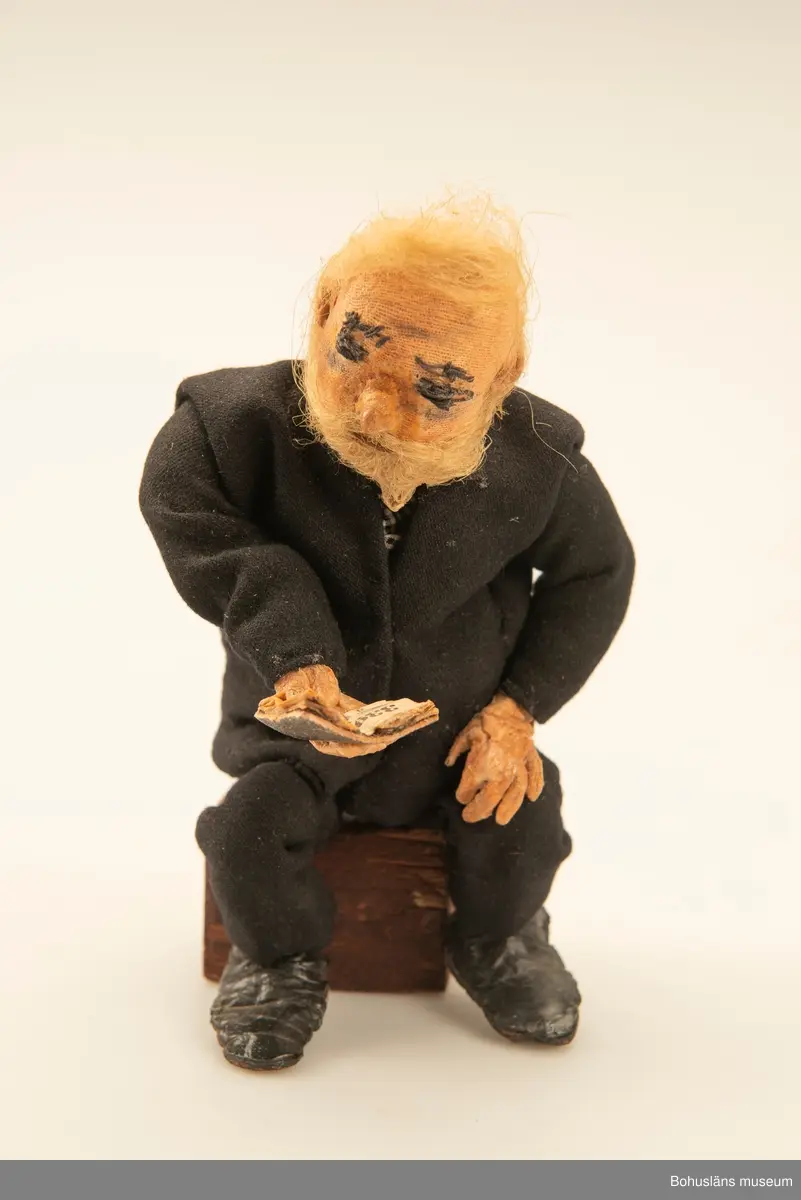 Gubbe med psalmbok sittande på en träkub