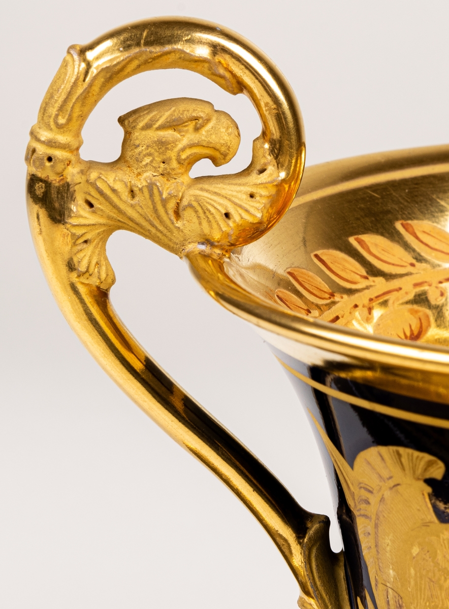 Karl XIII:S kopp.
Kopp med fat från Daite Freies i Paris, omkring 1800.
Koppens höjd 9.5 cm. Fatets diameter 16,5 cm.
Koppen bär på ena sidan Karl XIII:s bild och är på motstående sida dekorerad med ett par antika hjälmar.
Dekor i empirestil i guld och blått.
En grepe med örnhuvud och palmettdekor. Fatet är dekorerat med en eklövskrans.