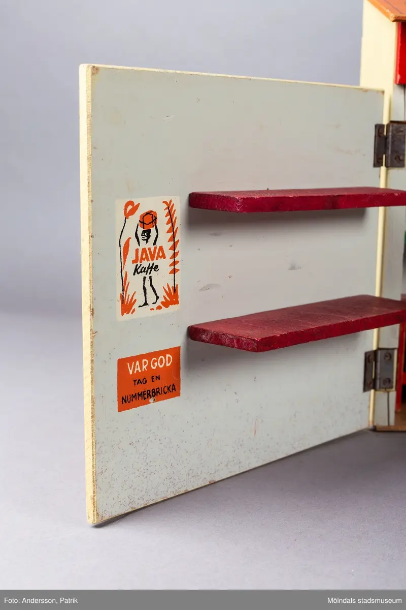 Leksak i trä i form av en liten affär. På framsidan finns texten "Kährs Diversehandel", dekor i form av två skyltfönster och en liten dörr med ett handtag i metall. Fronten består av två luckor går att öppna. Inuti finns en butiksinredning med gröna hyllor och en lös röd butiksdisk med sex gula utdragbara lådor.
Allt är tillverkat i trä. Affärens utsida är målad i en ljusgul färg, med ett tak som är bemålat med tegelröda tegelpannor. Under takåsen löper en röd list med texten "Kährs Diversehandel" målat med vita bokstäver.
Leksaksbutiken är tillverkad av Kährs. Företaget grundades 1857 och tillverkade till en början leksaker och möbler, men tillverkningen övergick efter andra världskriget alltmer till att omfatta endast dörrar och golv.