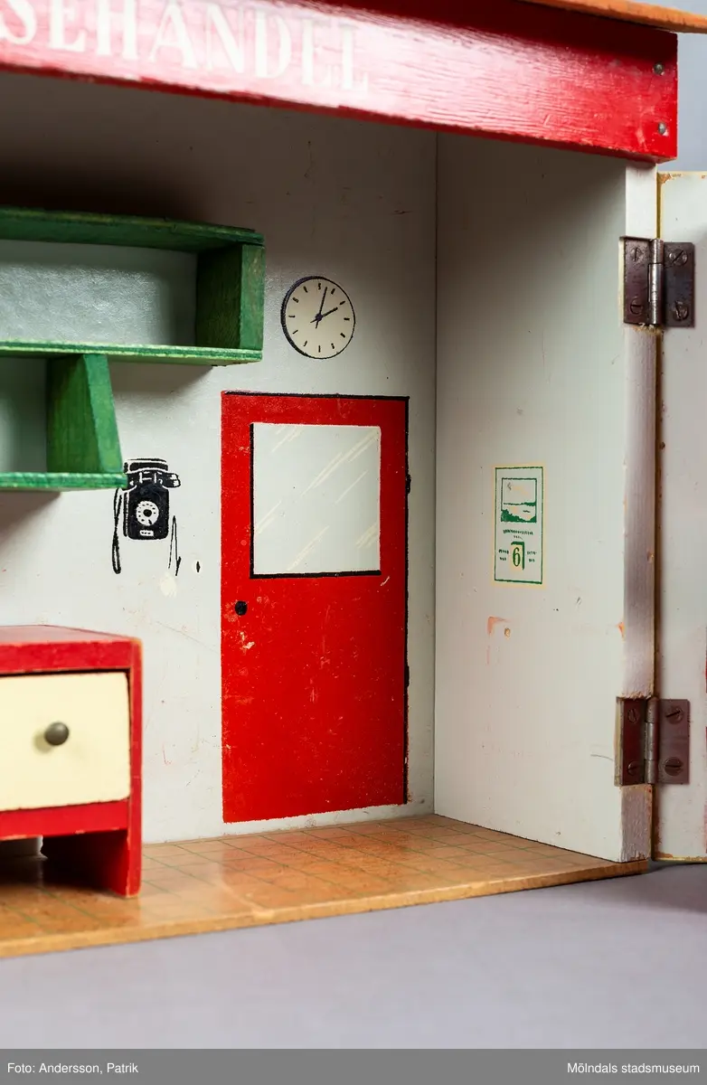 Leksak i trä i form av en liten affär. På framsidan finns texten "Kährs Diversehandel", dekor i form av två skyltfönster och en liten dörr med ett handtag i metall. Fronten består av två luckor går att öppna. Inuti finns en butiksinredning med gröna hyllor och en lös röd butiksdisk med sex gula utdragbara lådor.
Allt är tillverkat i trä. Affärens utsida är målad i en ljusgul färg, med ett tak som är bemålat med tegelröda tegelpannor. Under takåsen löper en röd list med texten "Kährs Diversehandel" målat med vita bokstäver.
Leksaksbutiken är tillverkad av Kährs. Företaget grundades 1857 och tillverkade till en början leksaker och möbler, men tillverkningen övergick efter andra världskriget alltmer till att omfatta endast dörrar och golv.