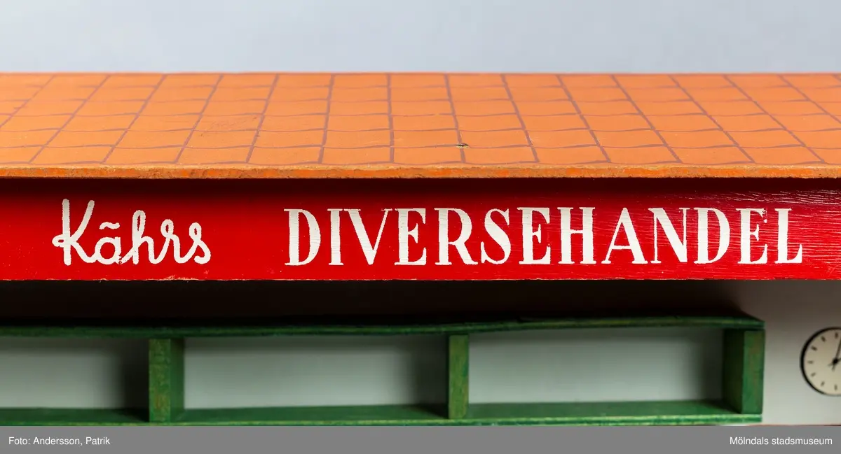 Leksak i trä i form av en liten affär. På framsidan finns texten "Kährs Diversehandel", dekor i form av två skyltfönster och en liten dörr med ett handtag i metall. Fronten består av två luckor går att öppna. Inuti finns en butiksinredning med gröna hyllor och en lös röd butiksdisk med sex gula utdragbara lådor.
Allt är tillverkat i trä. Affärens utsida är målad i en ljusgul färg, med ett tak som är bemålat med tegelröda tegelpannor. Under takåsen löper en röd list med texten "Kährs Diversehandel" målat med vita bokstäver.
Leksaksbutiken är tillverkad av Kährs. Företaget grundades 1857 och tillverkade till en början leksaker och möbler, men tillverkningen övergick efter andra världskriget alltmer till att omfatta endast dörrar och golv.