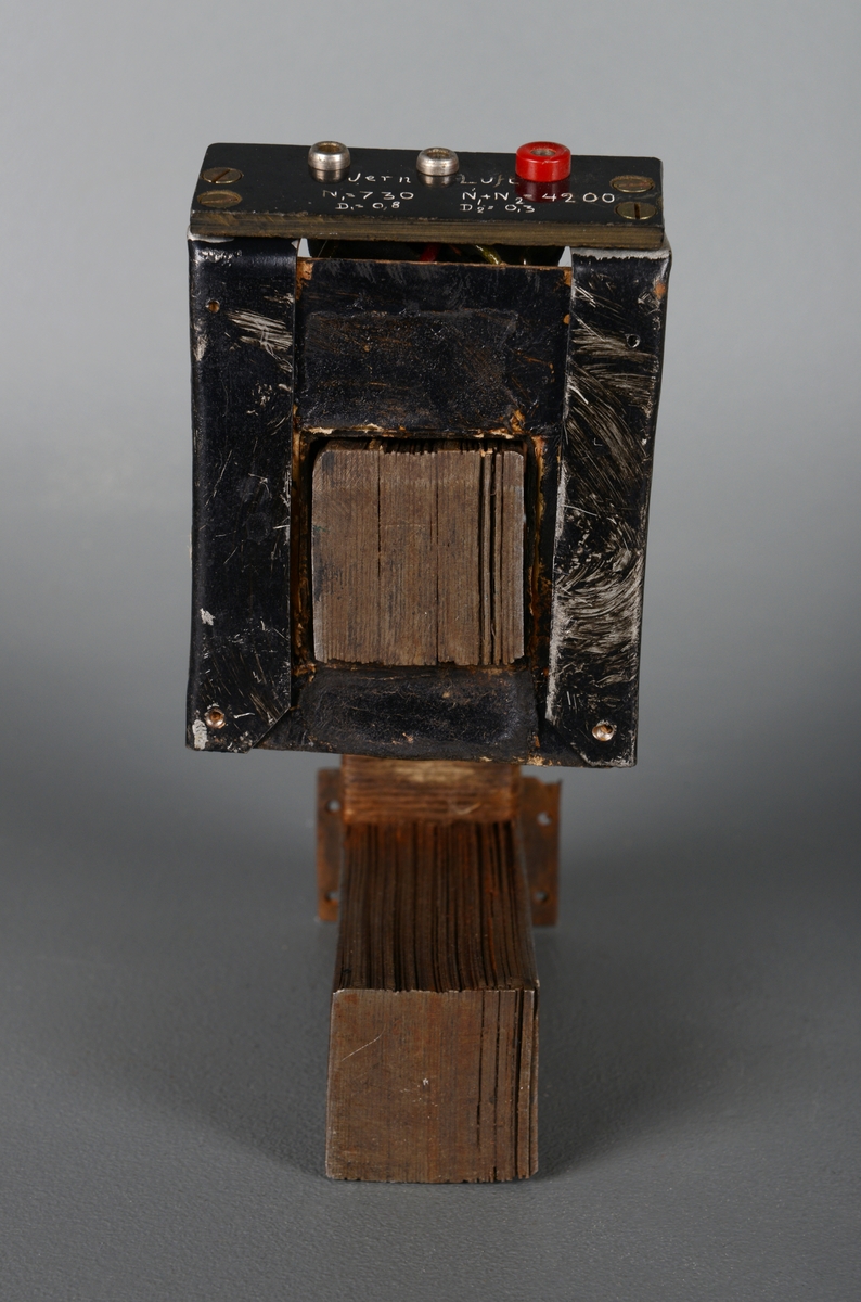 Et elektrisk element. Det er en firkantet ramme laget/satt sammen av mange, tynne metallplater. Det er liggende plater i bunn og topp, mens det er stående plater i kortsiden. Kortsiden i front er åpen. Platene er naglet/loddet sammen. Platene i kortenden er surret med hyssing. På toppdelen av rammen er det et element som kan tas av. Det er et kort rør trolig laget av metall som er kledd med papp festet/forsterket med hyssing. Det er en firkantet åpning som passer rammen av metallplater. I front pååe er det skrudd på et skiltt av svart plast. Det er tre uttak for å plugge i ledninger. Den helt til høyre har en rød plastring rundt seg, mens de to andre er av sølvfarget metall. På platen er det risset inn informasjon/formler.