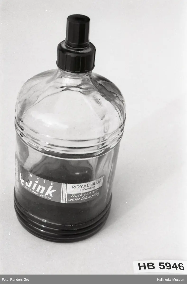 Flaske av blankt glas. Rett, sirkulært tverrsnitt. Det er litt blekk på flaska. Skruvekork av svart plast.