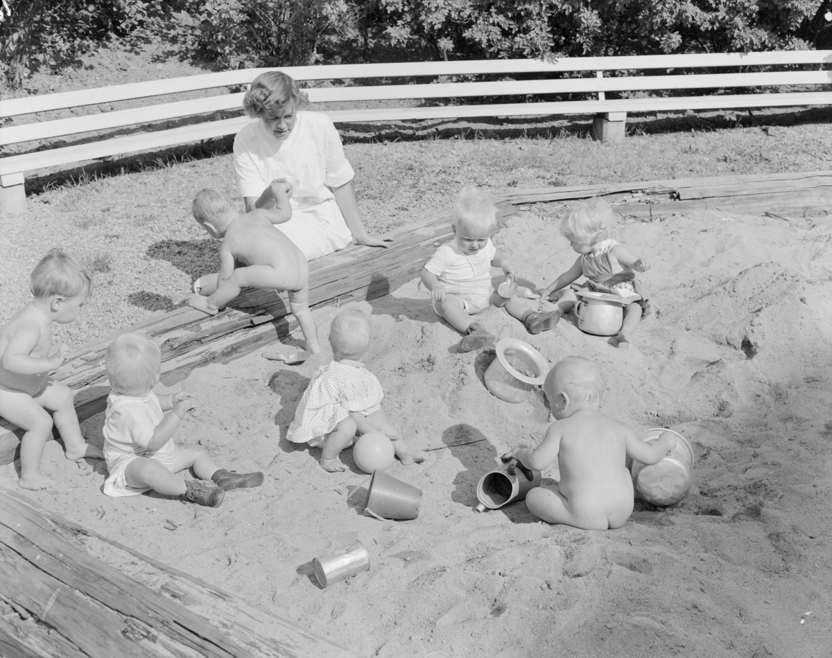 Fotografi av barn som leker i sandkasse og ansatte på Aline spebarnshjem.