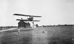 Flygplan Albatros NAB 9 landar på Malmen, omkring 1919-1925. I bakgrunden syns landsvägen mot Malmslätt och Röda och Gula förråden.