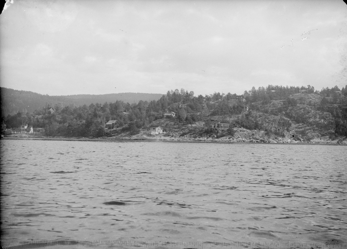 Landskapsbilde tatt fra båt mot et tettsted, sannsynligvis Svelvik. Tekst fra Teigens katalog: "Svelviks Historie, Svelviks museum etc. se også: Drammens Tidende, se også: Hurum Bygdebok 4938"