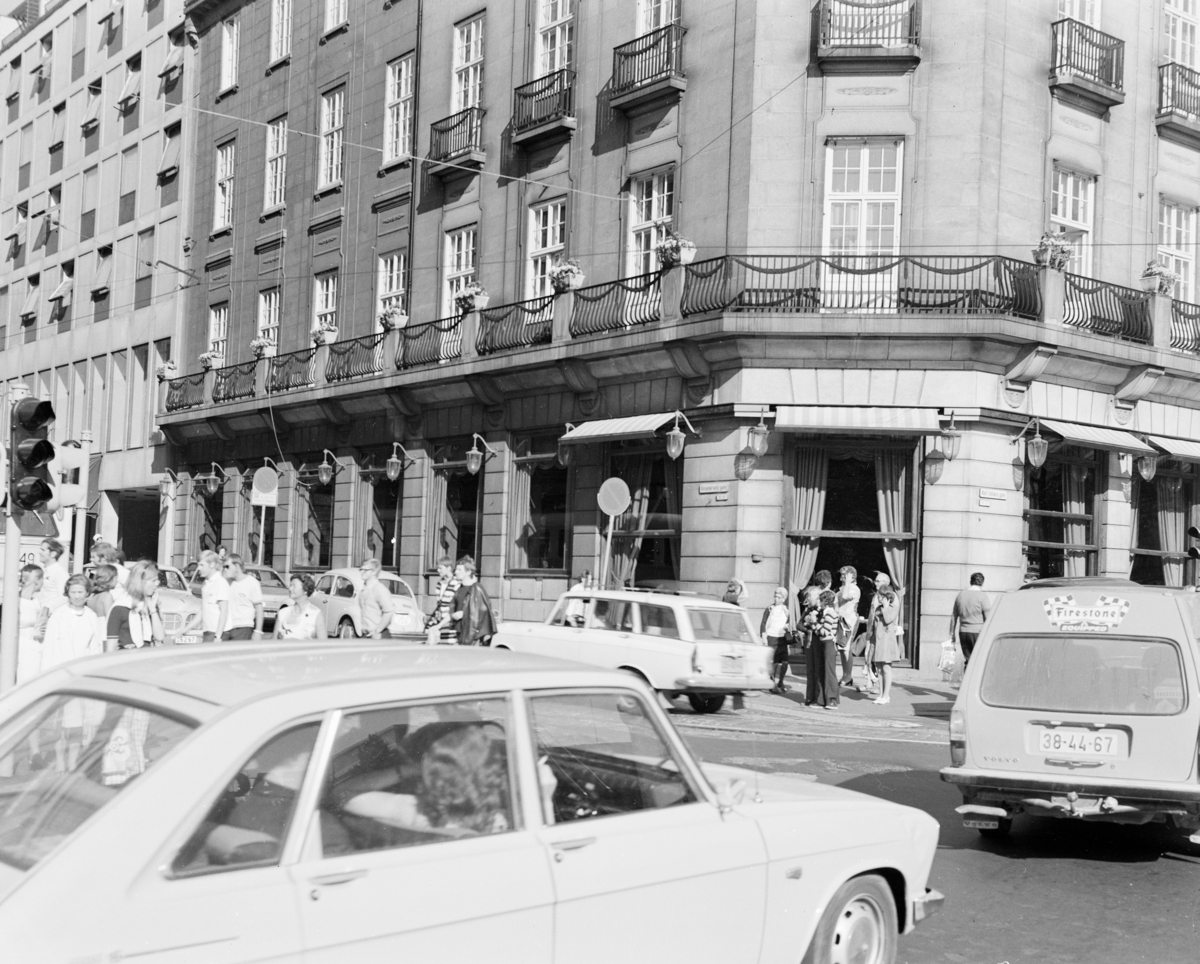 Biler og mennesker i gata på hjørnet av Grand Hotel på Karl Johan.