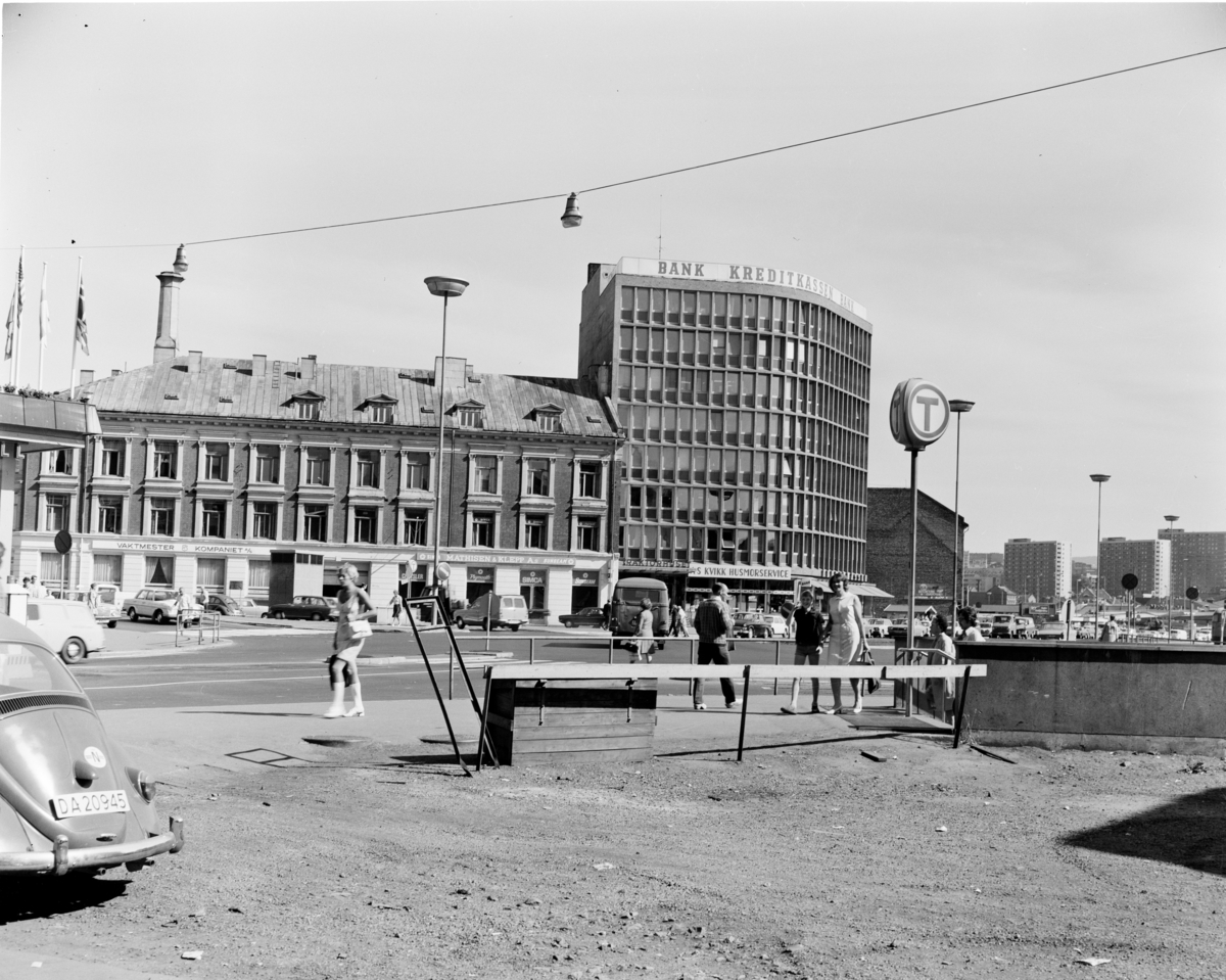 Jernbanetorget før byggingen av Oslo City og Oslo Plaza.Skiltene på husene i bakgrunnen forteller om forretningsvirksomhet som "vaktmesterkompaniet", "Kvikks husmorservice", "Kredittkassen", og et skilt med en stor T viser veien ned til T-banen. I bakgrunnen ses høyblokkene på Enerhaugen, som ble ferdigbygget av OBOS i 1965.