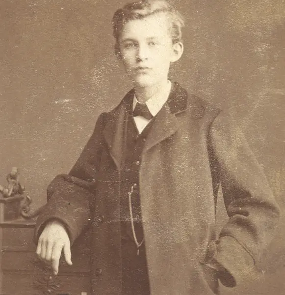 Ung Edvard Munch, står penkledd og lener seg til en kommode