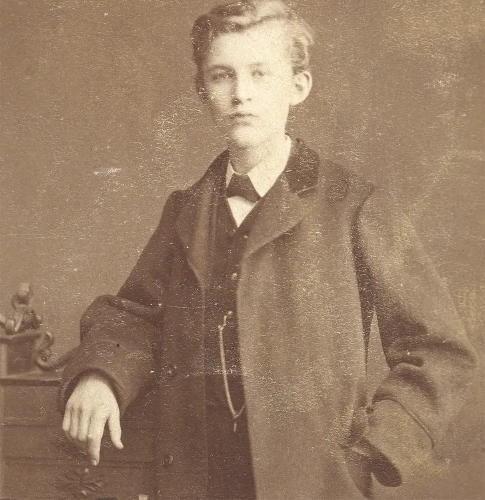 Ung Edvard Munch, står penkledd og lener seg til en kommode