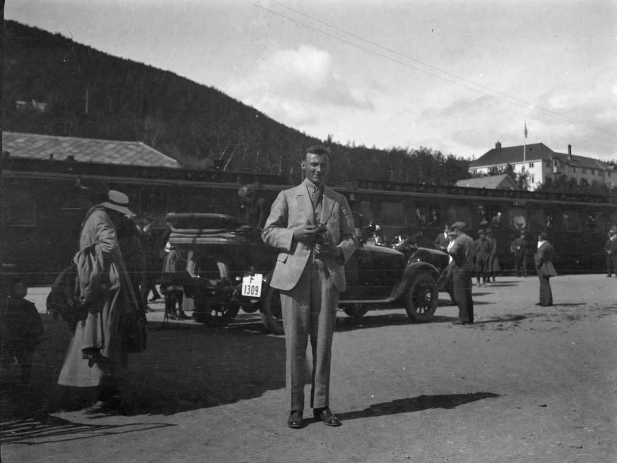 Fra jernbanestasjonen på Geilo med Dr Holms hotell i bakgrunnen. Mellom toget og en person i forgunnen er en kabriolet med registreringsnummer F 1309