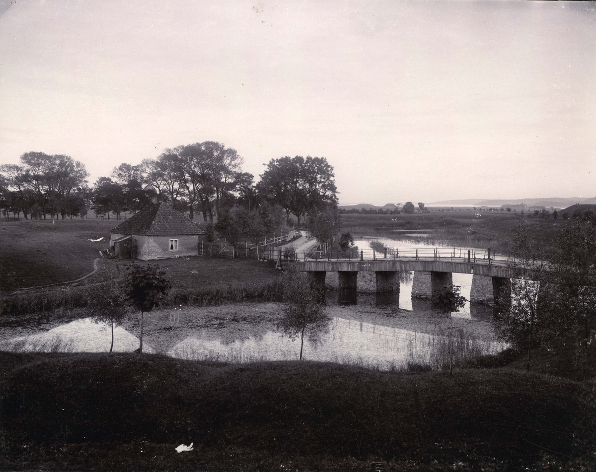 Fredrikstad. Østsiden. Gamlebyen. Vollgravene. Voldportbroen (Vindebroa). Ravelinet, Vaktstue. (Ravelin er er et festningsverk foran en kurtine, dvs. den rette delen av en festningsvoll, mellom to bastioner). I Gamlebyen er det fire kurtiner mellom de fem bastionene, blant dem vollravelinet (bildet) midt imot Voldportbroen og vollporten. Den første broen ble  ble bygd i 1667, Den var opprinnelig smykket med fargerikt malte trefigurer. Broen er fornyet en rekke ganger. Vaktstuen er fra 1740-tallet. - I bakgrunnen Gamlebyen, Øra og Kongsten.


Foto: Leverin