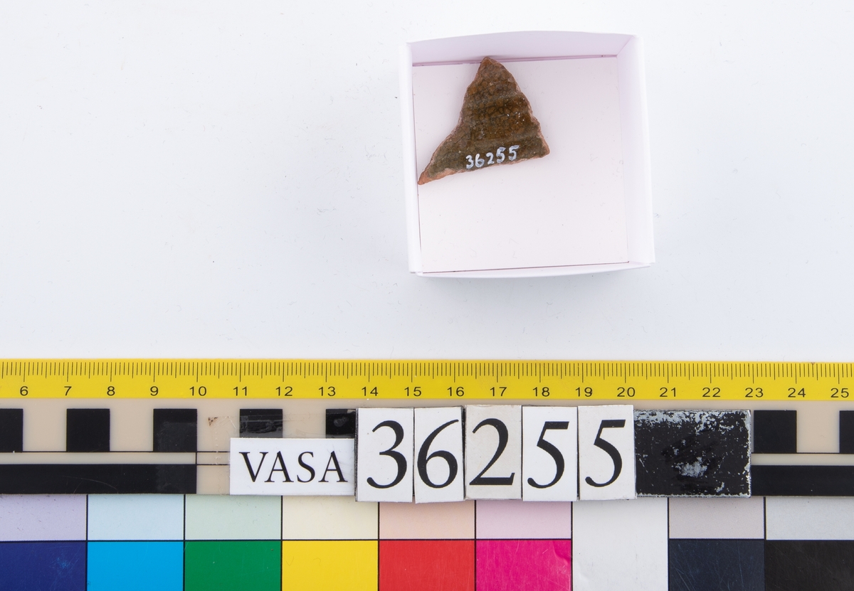 En keramikskärva. Räfflad. Brungrön glasyr på in- och utsidan.