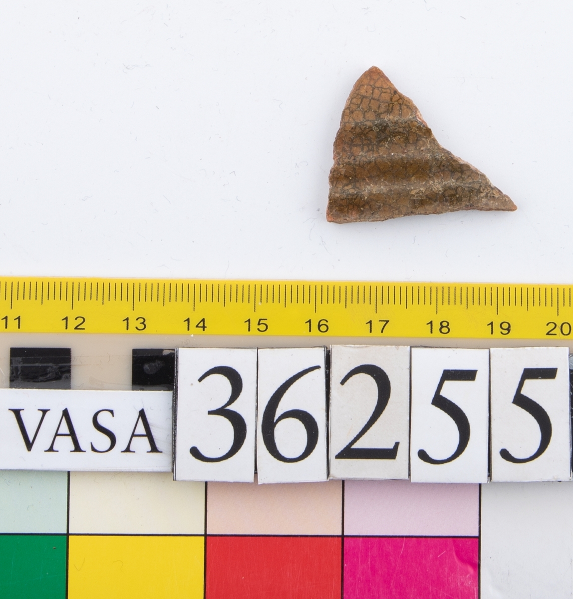 En keramikskärva. Räfflad. Brungrön glasyr på in- och utsidan.