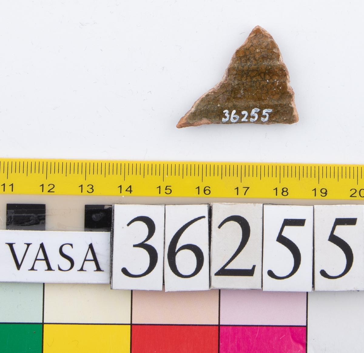 En keramikskärva. Räfflad. Brungrön glasyr på in- och utsidan.