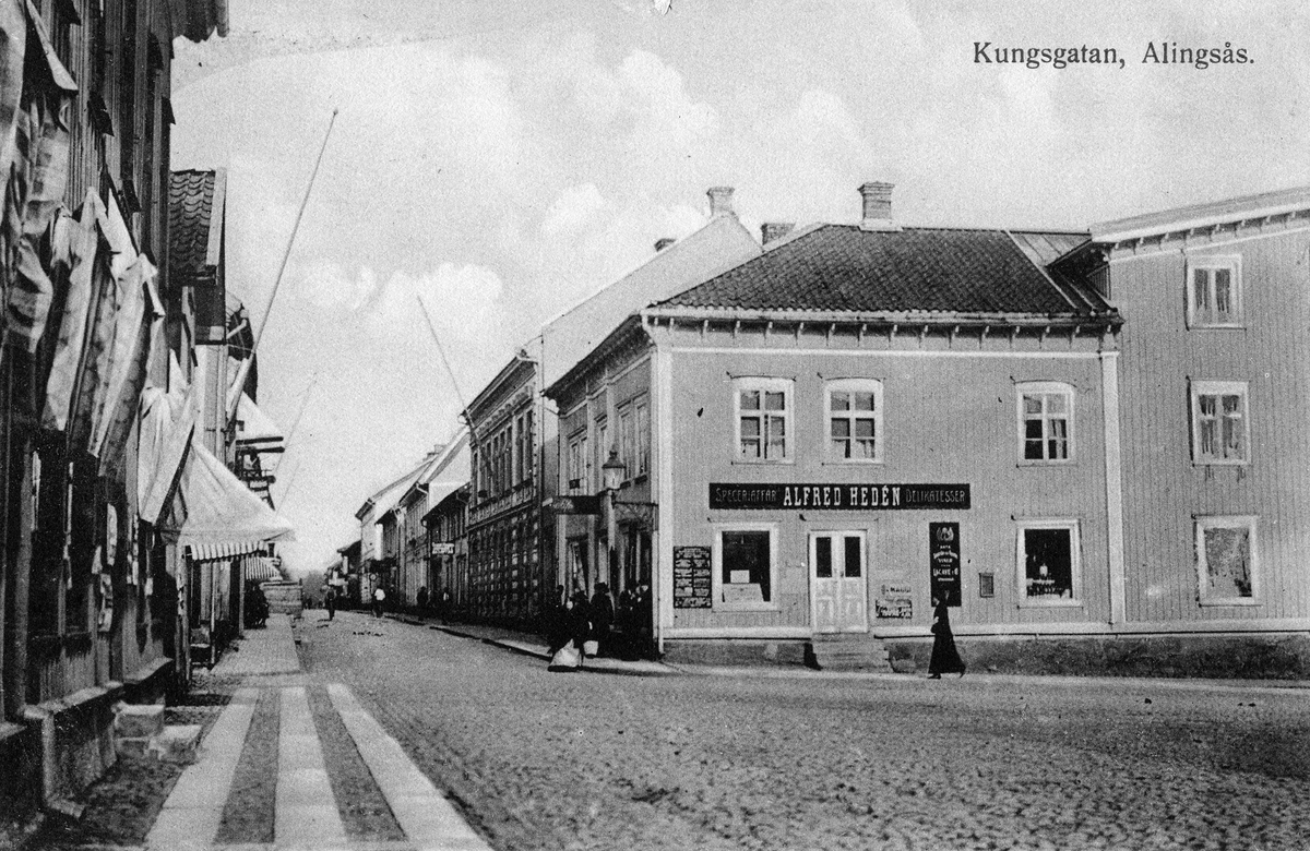 Vykort med motiv från Kungsgatan i Alingsås och Alfred Hedéns speceriaffär till höger i bild.