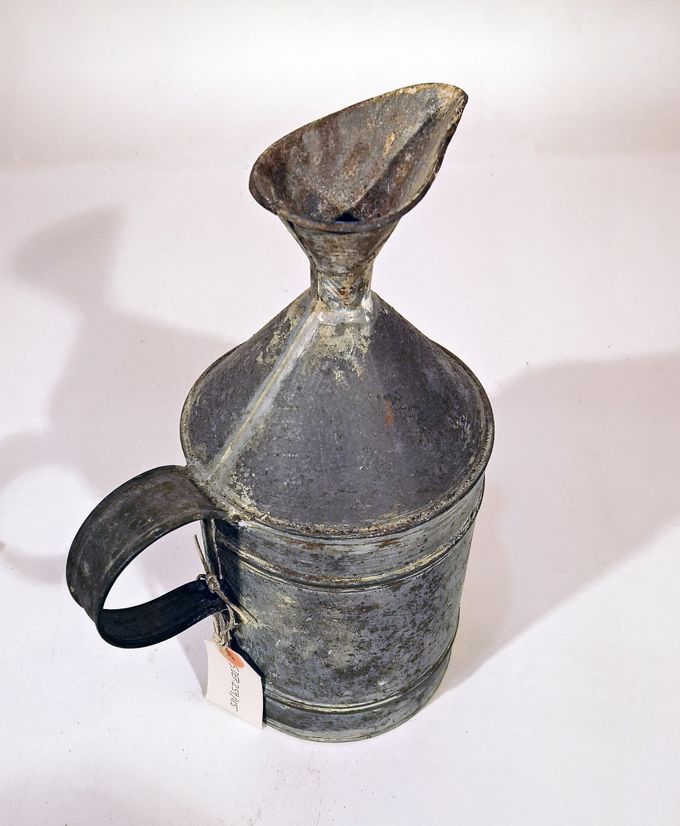 Fotogenkanna, "påfyllningskanna", av järnbleck. Cylindrisk form, med konisk överdel, påfyllningsöppning med trattformig avhällningsläpp. Handtag placerat på den cylindriska sidan, utan bärbygel. Rymd ca 5,5 l.