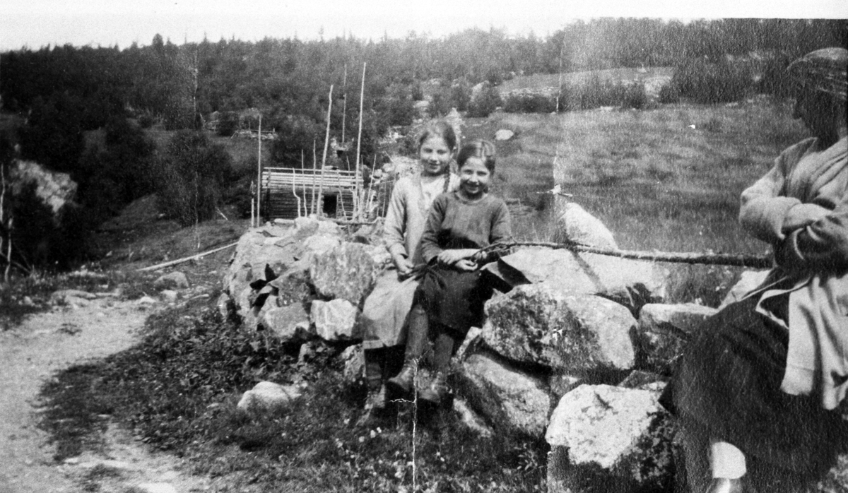 Mur som var ved sida av den gamle vegen gjennom Thorpegardane. Bildet er take like ovanfor Jevne garden. På muren sit frå venstre Ingrid Jevne og Guri Jevne. Den vaksne dama er ukjend