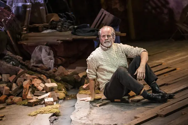 En teaterscene: En mann sitter på gulvet i rufsete omgivelser. 
