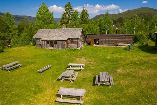Et tun med to gamle tømmerbygninger og samling benker på plenen i forgrunnen