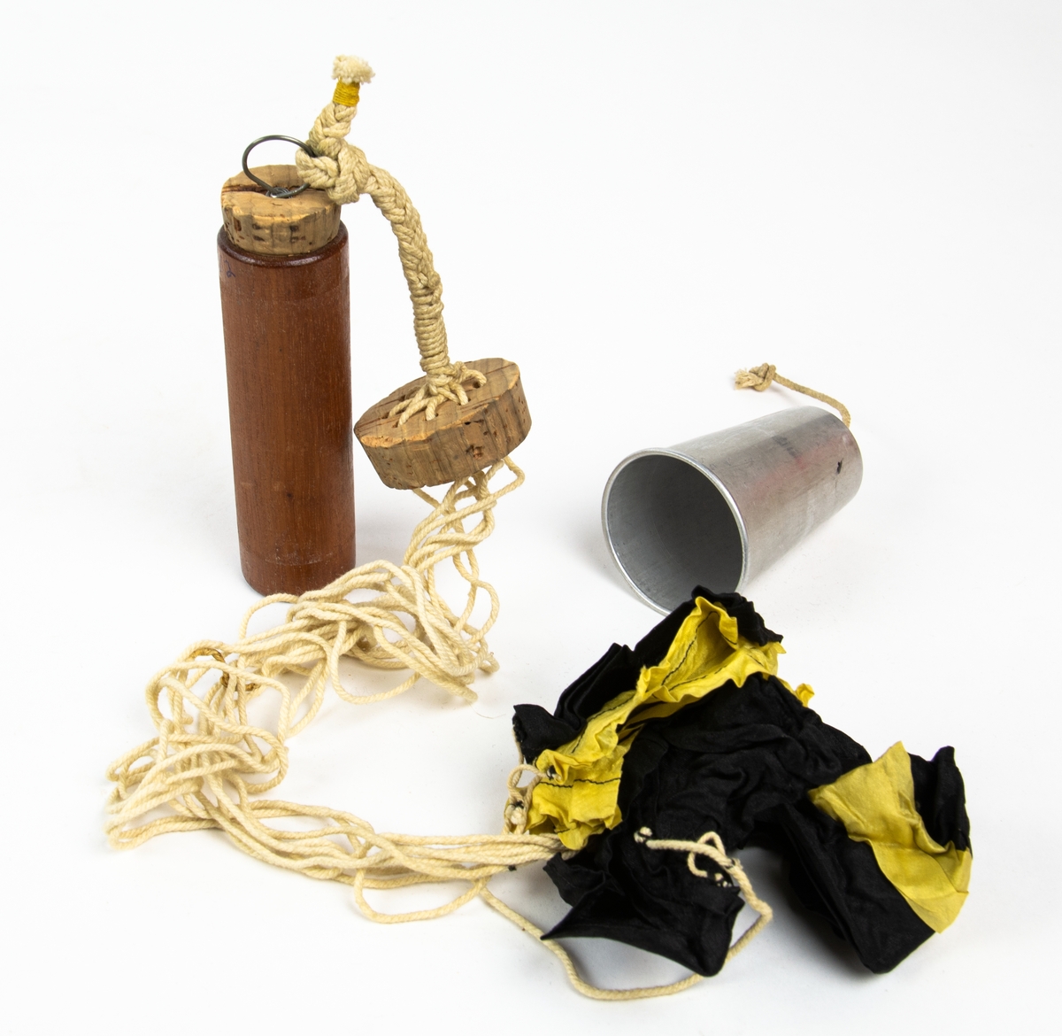 Miniatyrfallskärmar, dokument och läderdetaljer.
Bild 1-3: Träcylinder med korklock sammanlänkad med en metallkopp innehållande en miniatyrfallskärm. Cylindern är fylld med sand.
Bild 4: Träcylinder med korklock, utanpå text enligt Följande: "Minne Från K.S.A.S:s tävlan med mintayrfallskärmar vid Saltsjöbaden den 23 Juli 1920. Denna fallskärm tillhör Löjtnant Thor Thörnblad Strandv 78 Sthlm." 
Bild 5: Annons "Flygafton å Saltsjöbaden", urklippt ur oidentifierad dagstidning.
Bild 6: Etikett för cylinder.
Bild 7-8: Dokument
Bild 9: Läderremmar med präglad text. Tre läderbitar präglade "TRE KRONOR", "MODELL I" och "MODELL II" en rem med texten "Carry here".