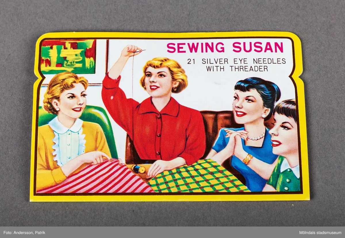 En förpackning med synålar från Japan. Förpackningen innehåller synålar. På framsidan finns en bild på fyra kvinnor som sitter och umgås och syr.