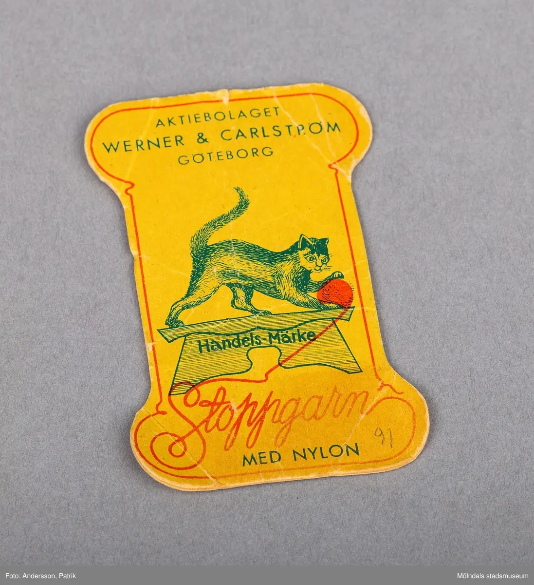 En pappskiva för stoppgarn. Skivan är gul till färgen med en röd snirklad inramning. Den 1 April 1885 grundade Gustaf Werner tillsammans med en jämnårig kompanjon, Wilhelm Carlsström, företaget Werner & Carlström för engrosförsäljning av textilvaror, främst garn av ylle och bomull. Firmans stoppgarner känna igen på en liten katt som leker med ett nystan.