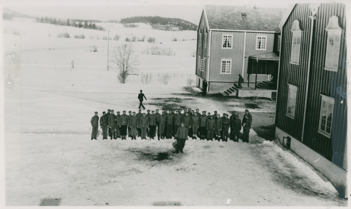 En del av "Trondheimsgislene" på Falstad i 1942, fotografert på gårdsplassen på Falstad nedre (Falstad skolehjem). Bildet er tatt fra bestyrerboligen, trolig av skolehjemsbestyrer Hans Harstad. Gislene kom til Falstad i mars 1942, og ble overført til Falstad nedre ("Øvergården") etter å ha vært en periode i leirens hovedbygning.