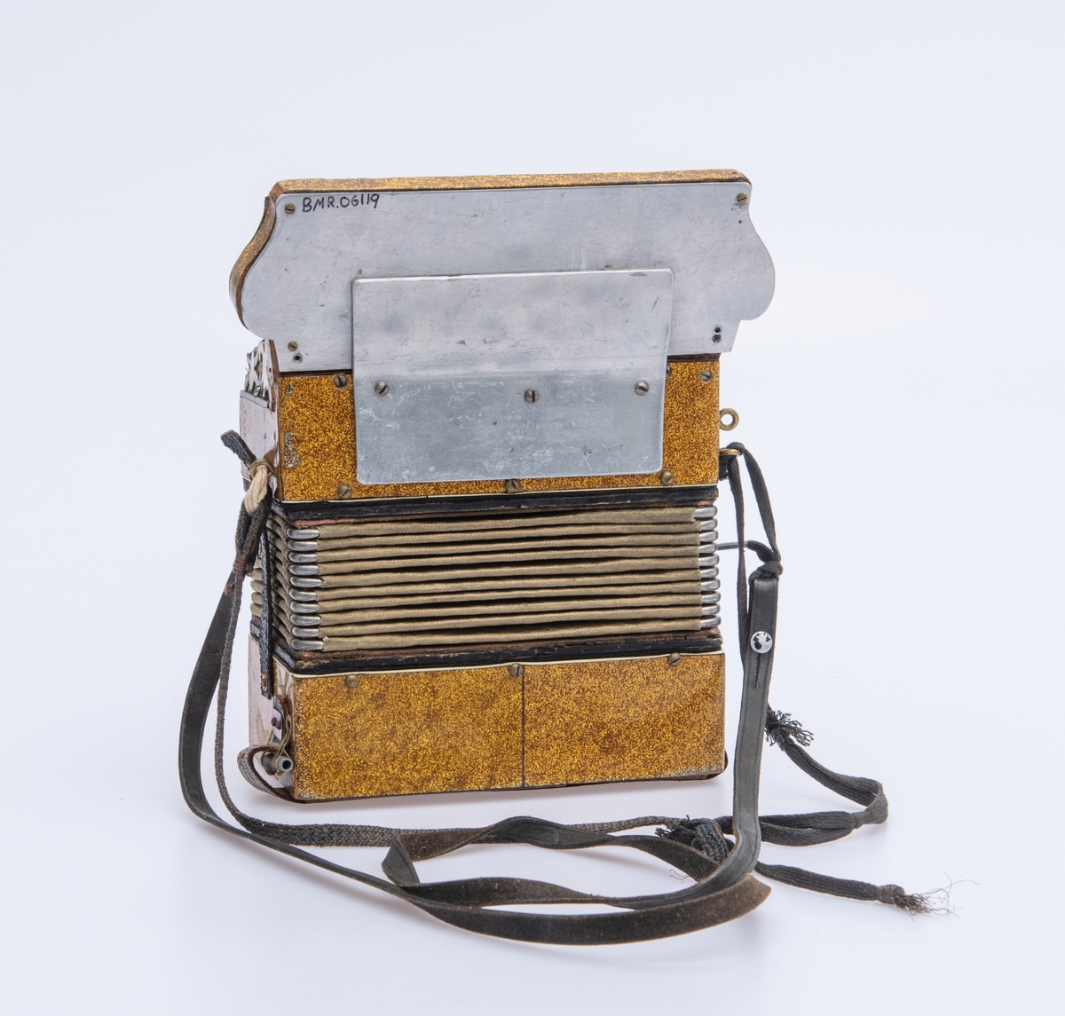 Gullspraglete overflate, med innsatte pyntejuveler. De fleste mangler. Blankt metallbeslag over knappene på høyre side foran. Lærreimer.