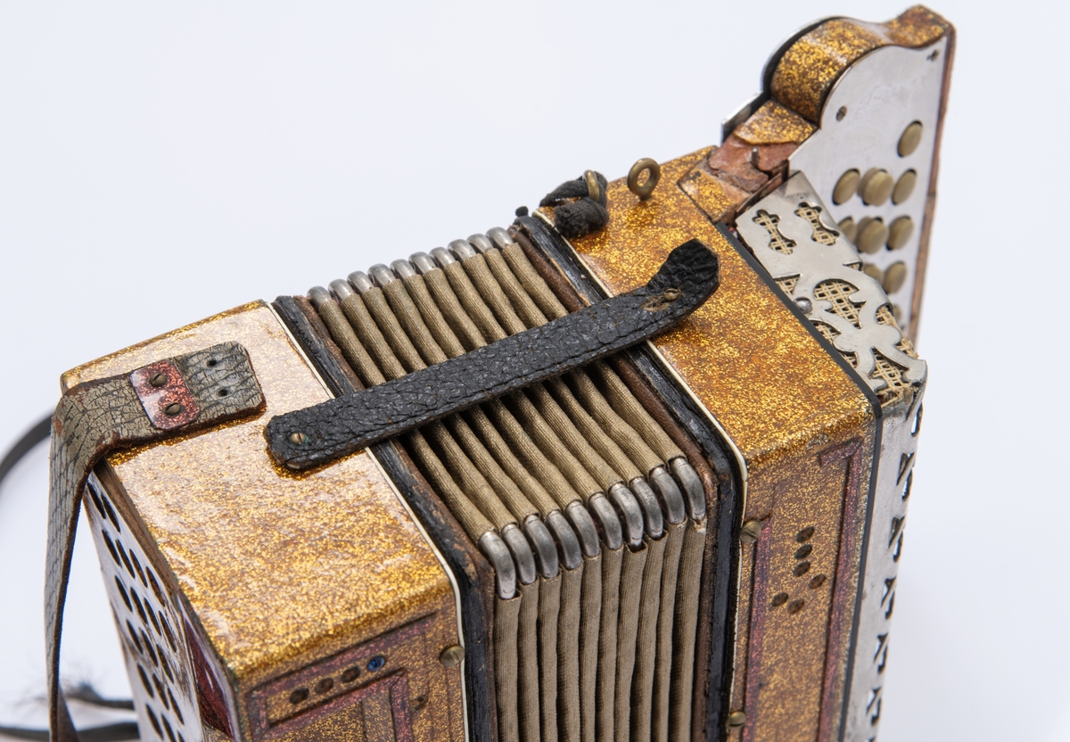 Gullspraglete overflate, med innsatte pyntejuveler. De fleste mangler. Blankt metallbeslag over knappene på høyre side foran. Lærreimer.