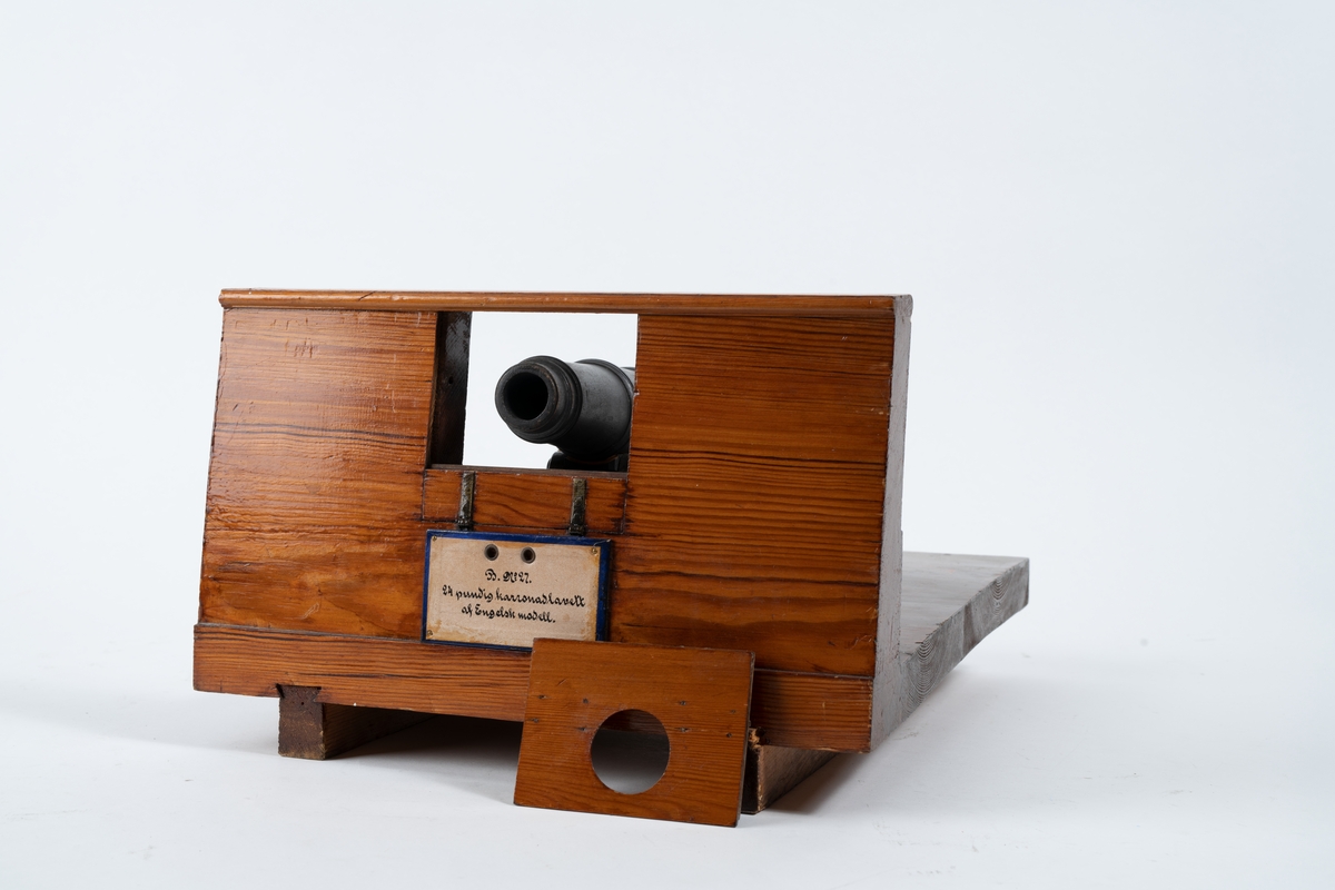 Kanonmodell: 24-pundig karronadlavett av engelsk modell, helt i trä, med karronad. Karronaden svartbetsad, lavetten fernissad. Lavetten L = 345 mm B = 310 mm H = 205 mm.