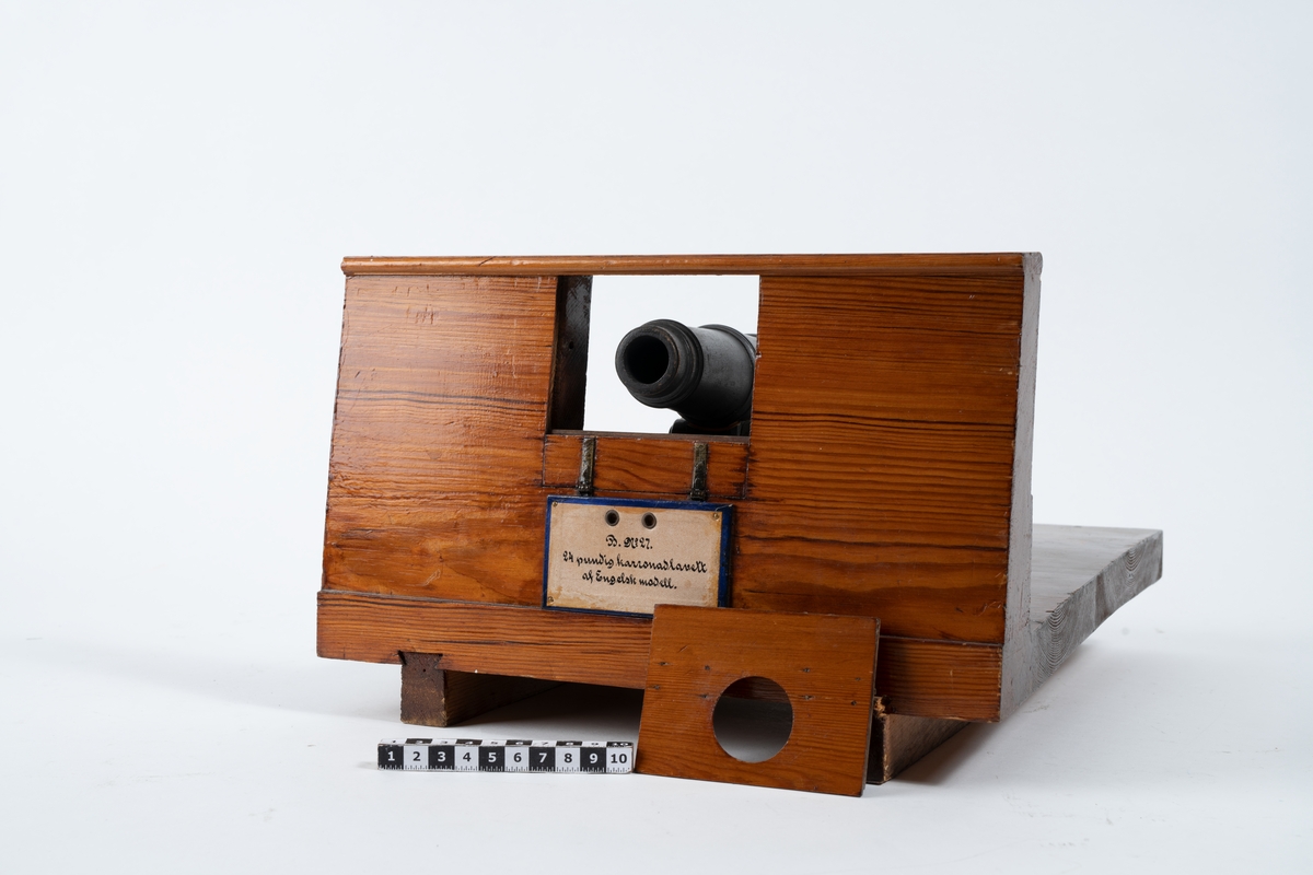 Kanonmodell: 24-pundig karronadlavett av engelsk modell, helt i trä, med karronad. Karronaden svartbetsad, lavetten fernissad. Lavetten L = 345 mm B = 310 mm H = 205 mm.