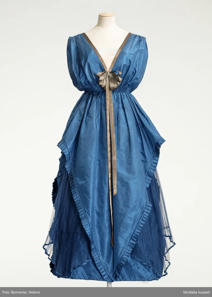 Ordered by Dora Lamm née Upmark (1880–1959), lady of the manor with a keen interest in innovative art and fashion. Delivered 1919.
A silk taffeta and pleated chiffon creation with gold ribbon details. Dora Lamm was married to the art collector Carl Robert Lamm of Näsby Manor, Täby. She embraced the Arts & Crafts movement and knew many artists such as Carl and Karin Larsson.