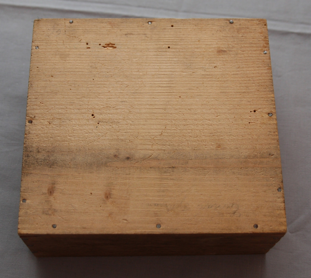 Bygglåda, rektangulär låda av furu med inskjutbart lock från Gemla Leksaksfabriks Aktiebolag (1866-1884). Utan leksaker innuti. Etikett på locket som föreställer en logga med en gunghäst omgiven av tre vita blommor. Etikettens yttre kanter har ett dekorelement föreställande ett slingrande band.