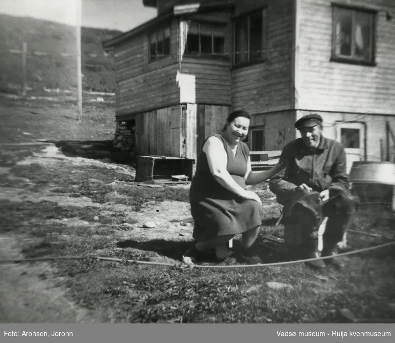 Elna og Håkon Aronsen har en "pust i bakken" foran deres hjem på Makkenes i Vadsø kommune ca 1970. Håkon har sjøstøvlene på og har enten vært på sjøen eller skal på sjøen.