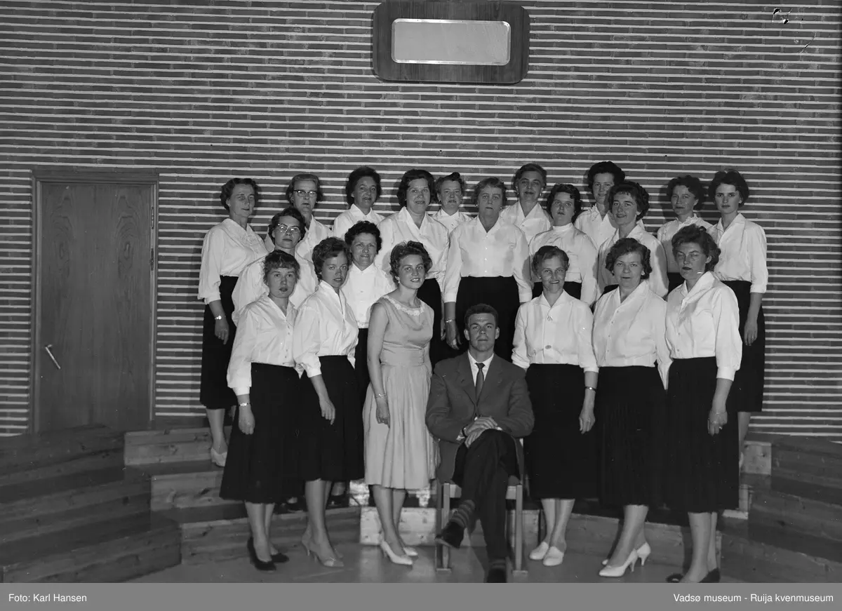 Vadsø Damekor 28. juni 1960. Damekoret med dirigent samlet til fotografering i Store studio på NRK-huset i Vadsø.
Øverst fra venstre 1.Klara B.Pettersen, 2. og 3 ukjent, 4.Turid Bjørkli, 5.ukjent, 6.Elisabeth Esbensen, 5.Borghild D. Løkting, 8.Ellen Helfjord, 9. og 10.Gerd Nikolaisen,  11.Reidun Basma Pedersen,  12.Inger Johanne Helfjord Hofseth, 13. Karethe Sæther, 14.Hulda Onseng, 15., 16., 17. og 18.ukjent, 19.Mary Bohinen, 20. Alfhild Ballo, 21.Solveig Berge.