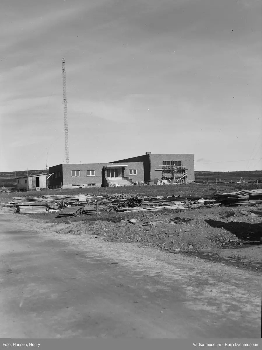 Det nye NRK-bygget i Vadsø ble reist 1948-49. Bygningen er ennå ikke helt ferdigstilt og vi kan vi se stillaser,  forskalingsmateriale, grushauger og arbeidsbrakke på og rundt bygningen. Bak bygget ser vi en av de 2 radiomastene.