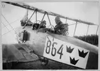 Flygförare och flygskytt på plats i flygplan Thulin FA märkt nummer 864 på marken. Vid skjutprov 1918.