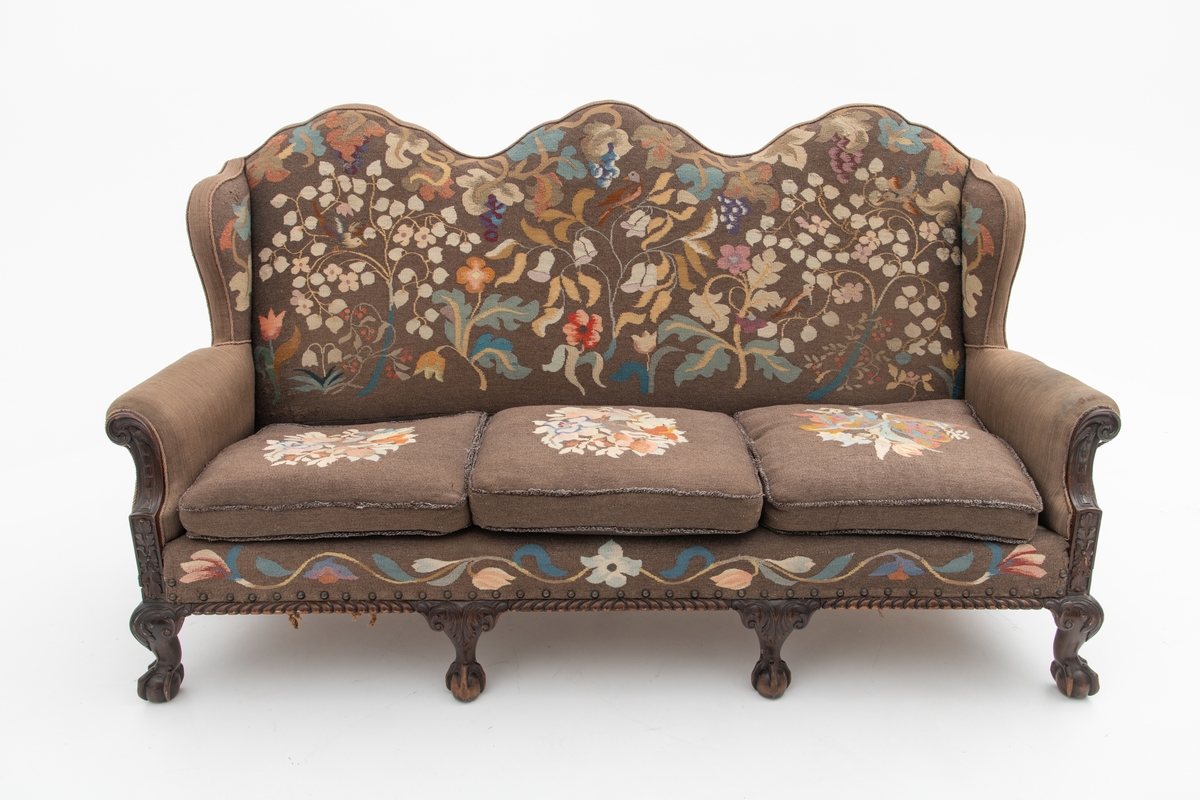 Sofa med trekk vevd av Ulrikke Greve. Vevnaden er vevet spesielt til denne sofaen. Det  er nyere stoff-trekk på armlenene. Møbeltrekket er nå stiftet fast med stiftemaskin; antagelig en reparasjon, og dekorert med pyntestift i messing.