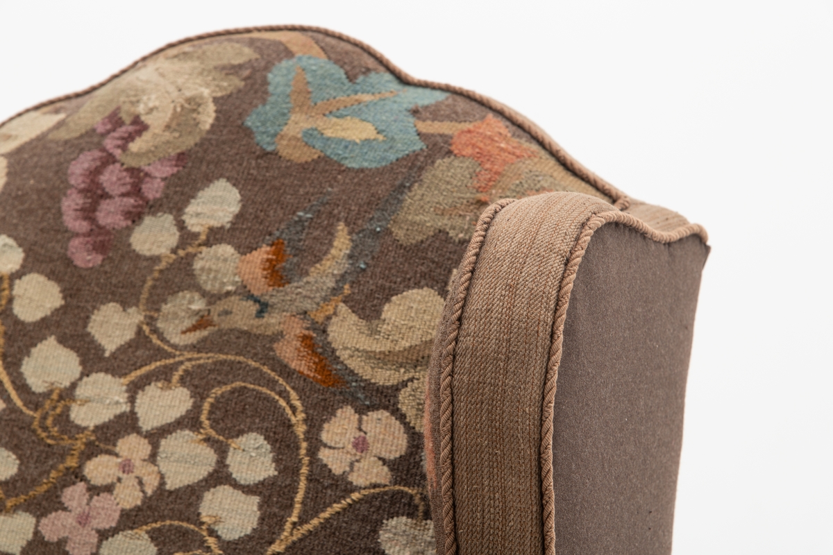 Sofa med trekk vevd av Ulrikke Greve. Vevnaden er vevet spesielt til denne sofaen. Det  er nyere stoff-trekk på armlenene. Møbeltrekket er nå stiftet fast med stiftemaskin; antagelig en reparasjon, og dekorert med pyntestift i messing.